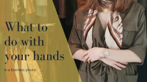 what to do with your hands in a business photo written in navy blue over a bright yellow, with a woman holding her hands across her body in a virtual business photoshoot